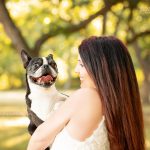 black and white small dog in woman's arms under trees in sunlight during dog photo shoot